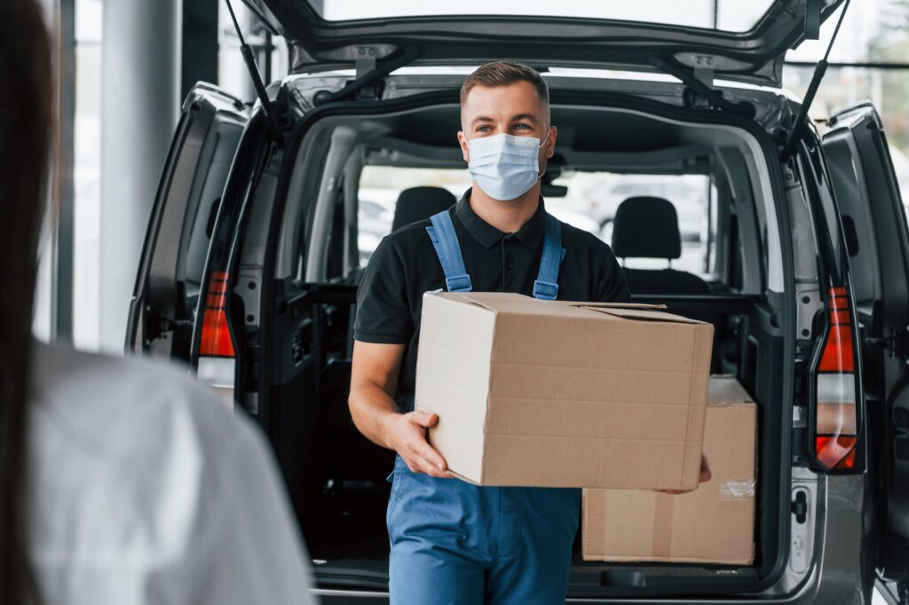 Woman waits for her order. Delivery man in uniform is indoors with car